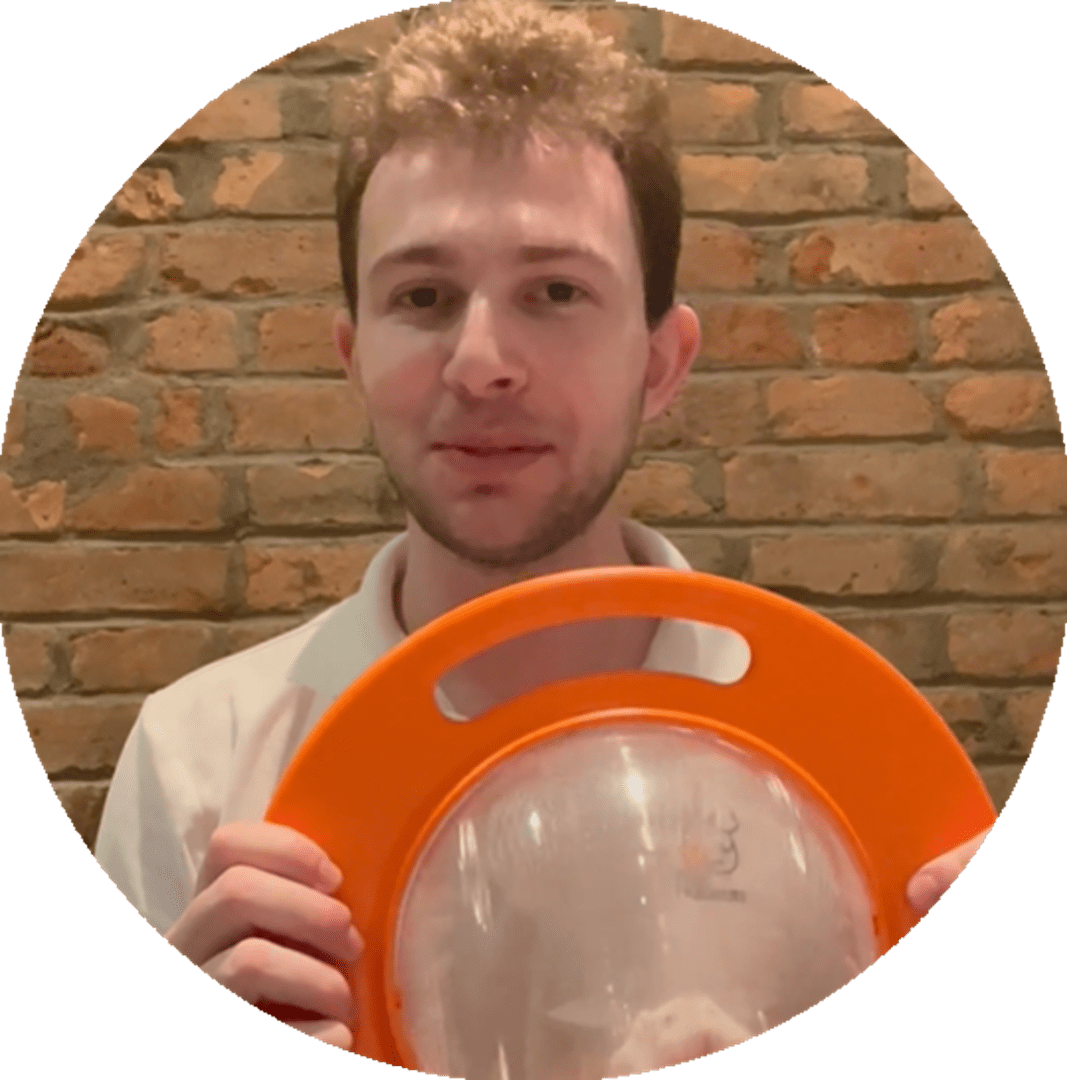 A man holding an orange frisbee in front of brick wall.